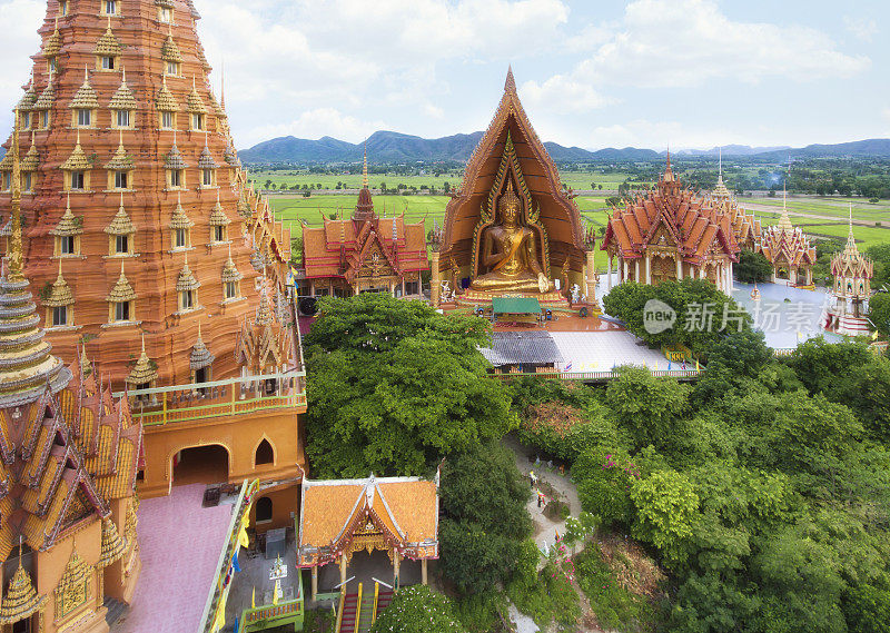 鸟瞰图(无人机拍摄)在Wat Tham Sua，泰国北碧府，金色的教堂和巨大的佛像和稻田